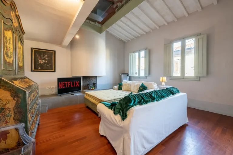 Sala luminosa con techo abovedado, sofá blanco, cojines verdes, mueble antiguo, TV con Netflix, y ventanas grandes.