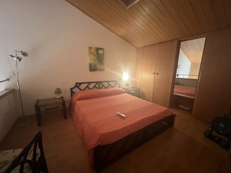 Habitación con techo de madera, cama doble con colcha naranja y cabecera negra. Mesitas de noche con lámparas, armario con espejo y luz tenue.