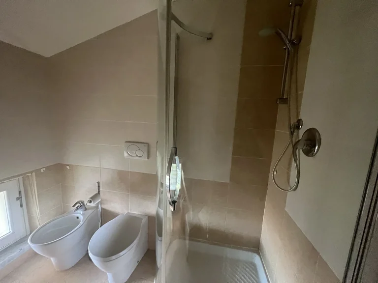 Baño moderno con ducha de cristal, inodoro y bidé. Lavabo sobre encimera y ventana baja con vidrio esmerilado. Iluminación empotrada en el techo.