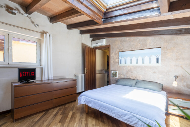 Habitación con techo de vigas de madera, cama doble, televisor con Netflix, ventana grande y luz natural.