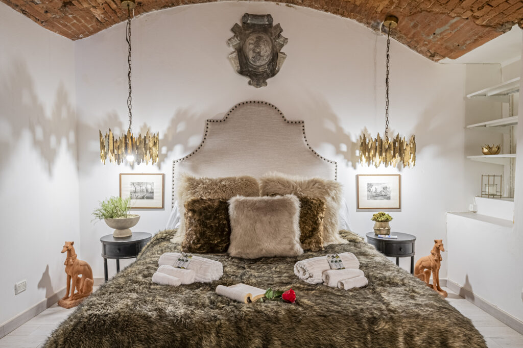 Dormitorio elegante con cama de peluche, lámparas doradas, figuras de perro y techos de ladrillo abovedados.