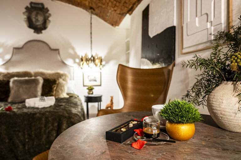 Habitación acogedora con cama lujosa, mesa con planta y café, pétalos rojos. Decoración moderna y elegante.