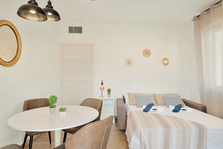 Sala moderna con sofá cama, mesa blanca con sillas marrones, decoraciones circulares en la pared y lámpara de mesa.