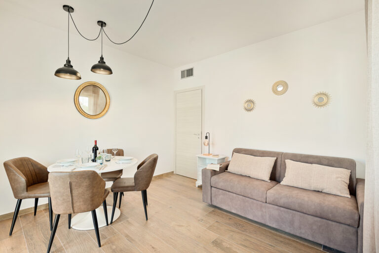 Sala de estar moderna con muebles marrones, mesa redonda con sillas, sofá gris, y lámparas colgantes negras.