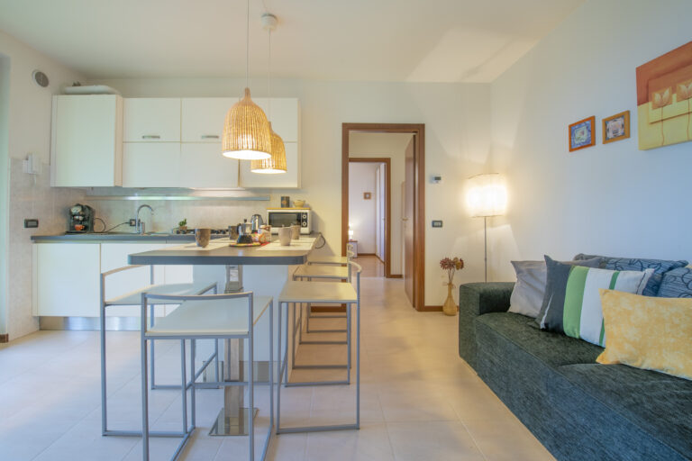 Cocina moderna con isla central, lámparas colgantes de mimbre, sofá verde con cojines y decoración de pared colorida.