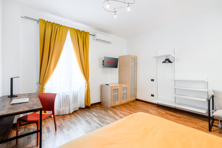 Habitación luminosa con cortinas amarillas, escritorio con silla roja, televisión con Netflix y aire acondicionado.