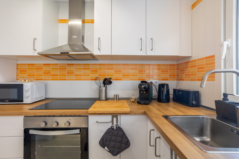 Cocina moderna con encimera de madera, azulejos naranjas, horno, microondas, cafetera y fregadero de acero inoxidable.