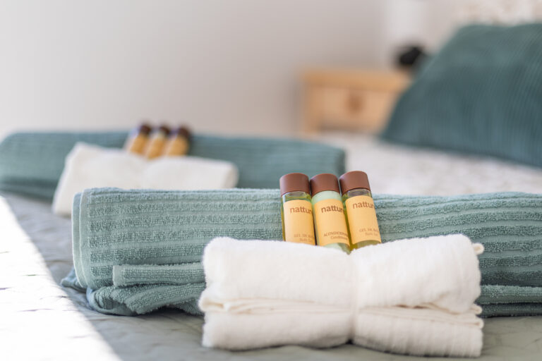 Toallas turquesa y blancas cuidadosamente dobladas con botellas de gel de baño y acondicionador sobre una cama.