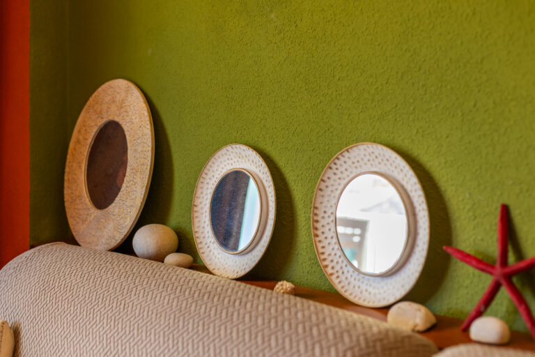 Tres espejos decorativos ovalados con bordes grabados, sobre estante verde, adornados con piedras y una estrella de mar roja.