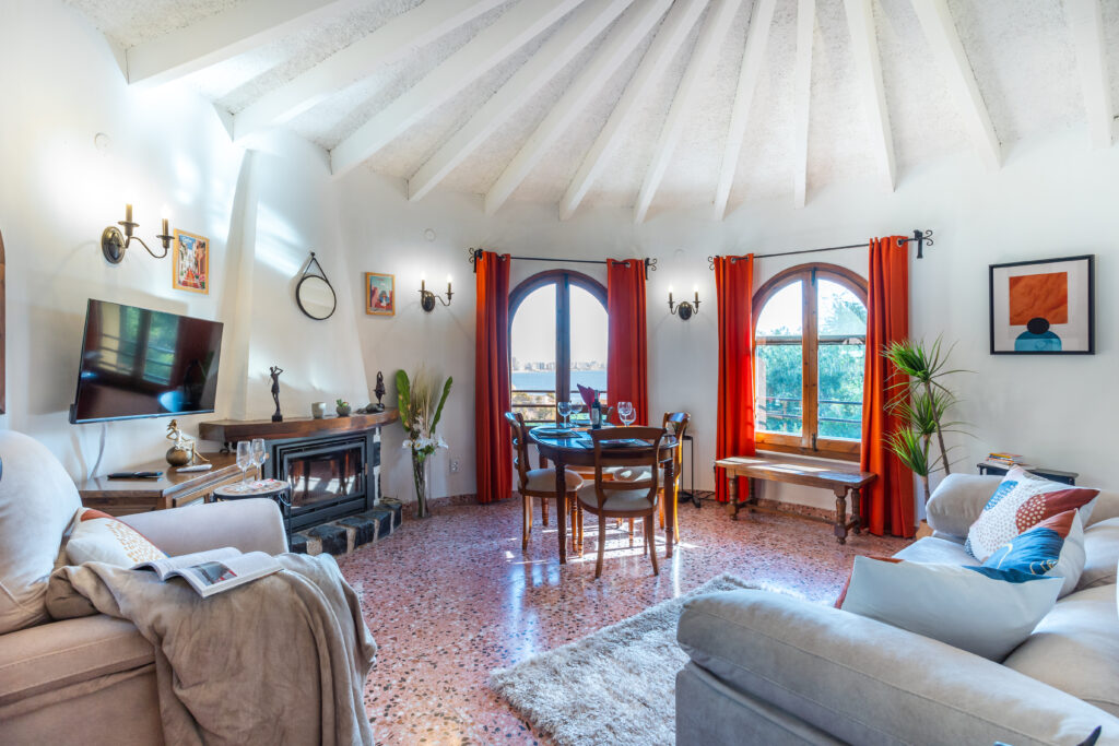 Sala de estar con techo abovedado, ventanas grandes, cortinas rojas, muebles acogedores y chimenea elegante.