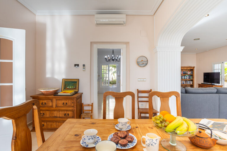 Sala de estar con mesa de madera, tazas y muffins. Frutero con bananas y naranjas. Aire acondicionado en la pared.